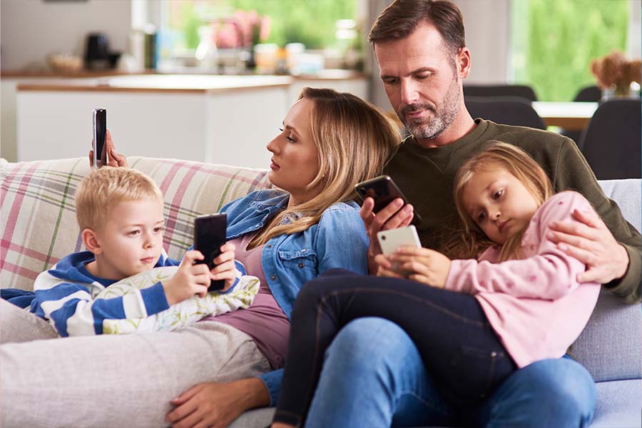 Family Connected Physically and Digitally. Sitting on a couch together but each holding a mobile phone device.